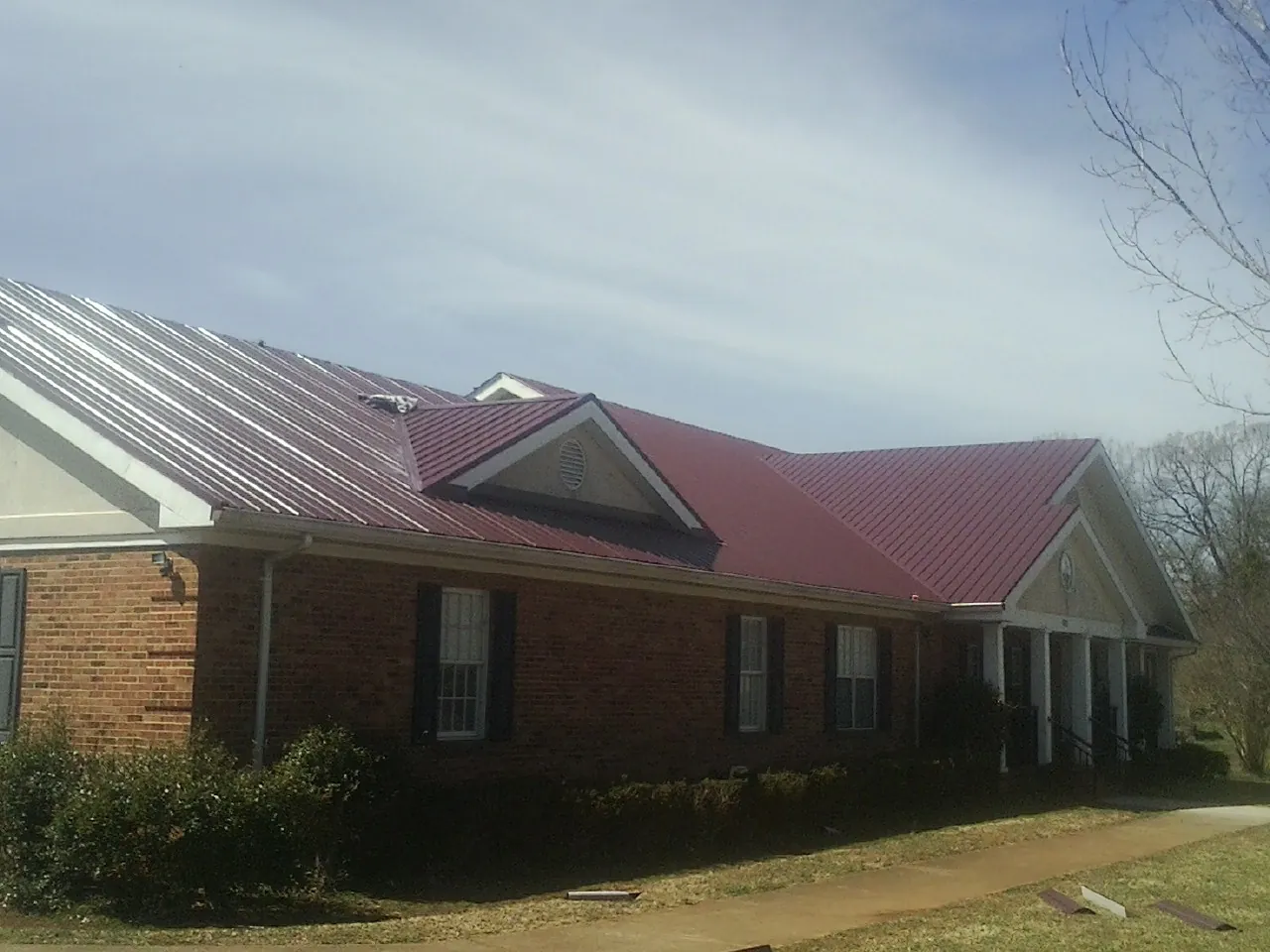 Red metal roof with gabled entries on a long brick building, from a Hail Damage Roof Repair job in Waimanalo