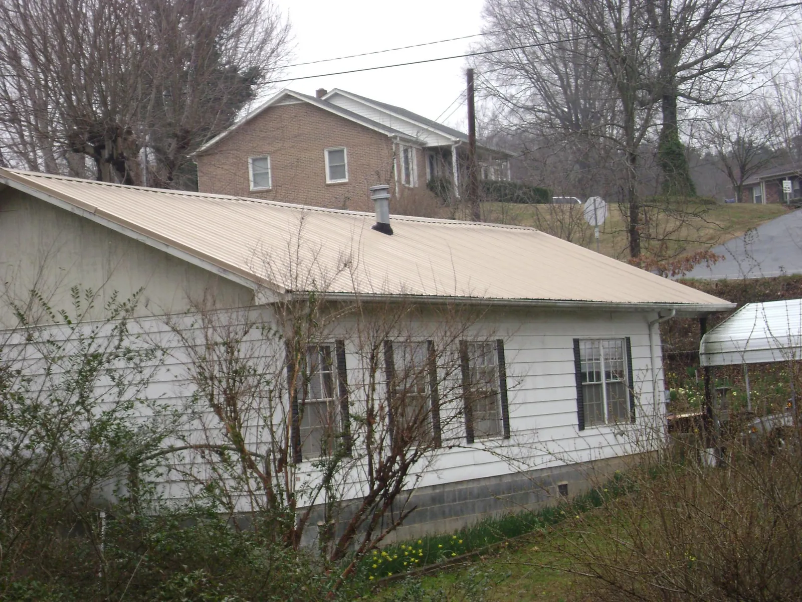 Tan metal roof on a white sided house set into a hillside — Commercial Roofing by Roofing Brothers in Waimanalo